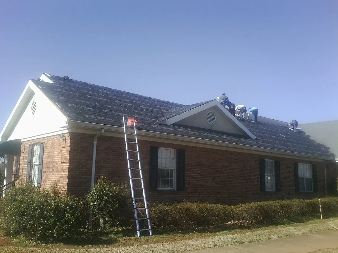Crew tearing shingles off a brick ranch roof with a ladder set — Metal Roof Repair work by our crew in Mount Enterprise