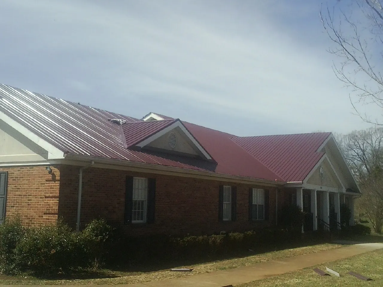 Red metal roof with gabled entries on a long brick building, from a Hail Damage Roof Repair job in Mount Enterprise