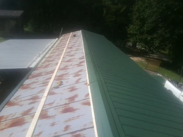 Old rusted panels beside newly installed green metal roofing — Wind Damage Roof Repair by Roofing Brothers in Mount Enterprise