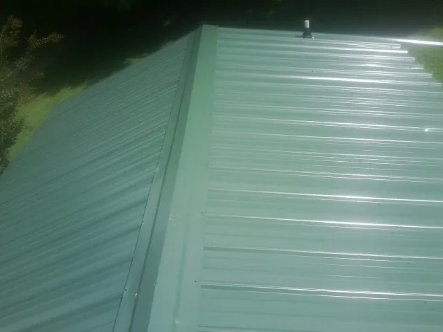 New green metal panels meeting at the ridge of a roof — Flat Roof Repair work by our crew in Mount Enterprise