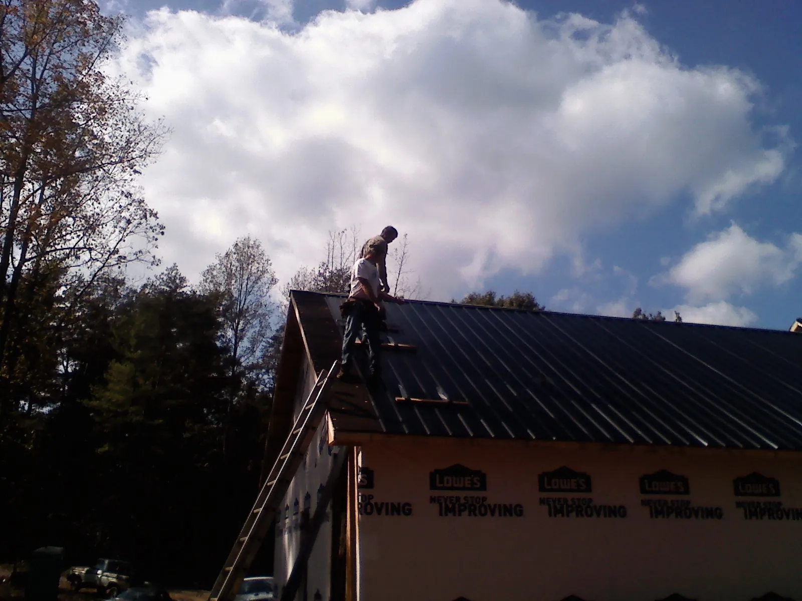 Roofer fastening dark metal panels high against a cloudy sky, from a Roof Inspection job in Mount Enterprise